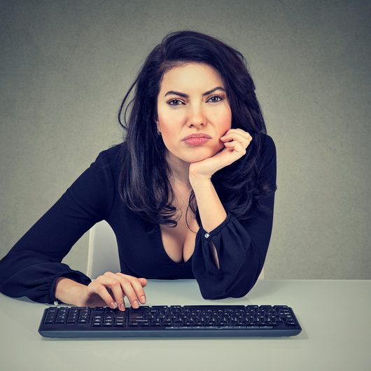 Young woman sitting at workplace and procrastinating being lazy and distracted feeling bored