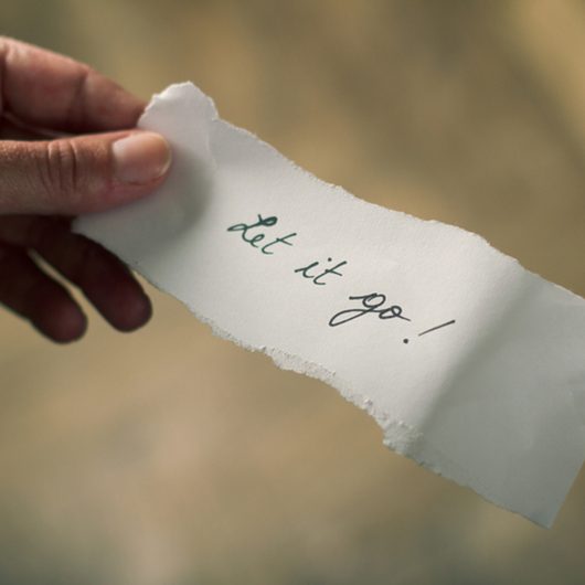 Hand holding a note of paper with the message let it go written on it