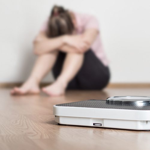 Weight loss fail concept. Scale and depressed, frustrated and sad woman sitting on floor holding head and arms on knees.