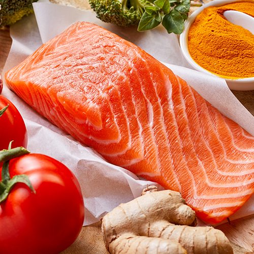 Nutrition for a healthy heart and cardiovascular system with fresh raw salmon rich in omega-3 fatty acids, tomatoes, turmeric, root ginger, stick cinnamon and garlic on a wooden table