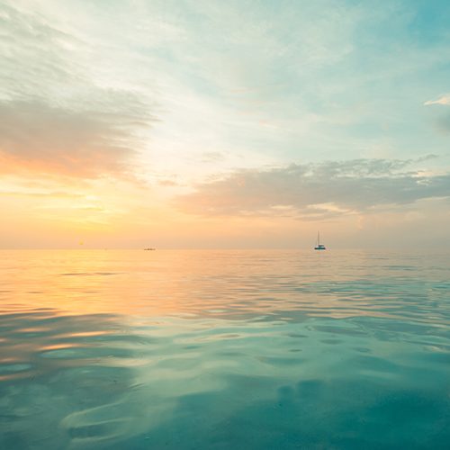 Look out on a calm blue sea with boat in the distance at sun rise