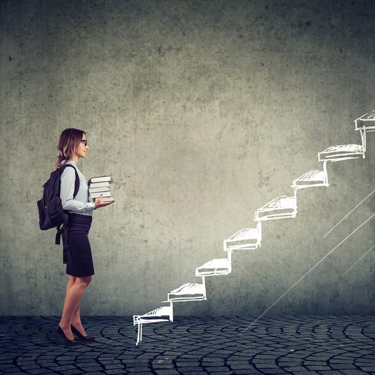 Female student with books standing on the stairs of education leading to success